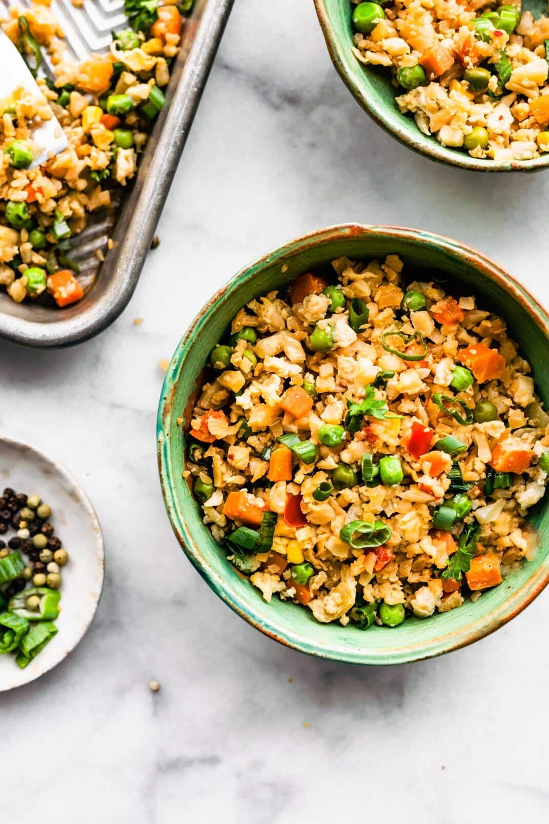 A bowl of Cauliflower Fried Rice on a counter with the rest of the fried rice on a sheet pan.