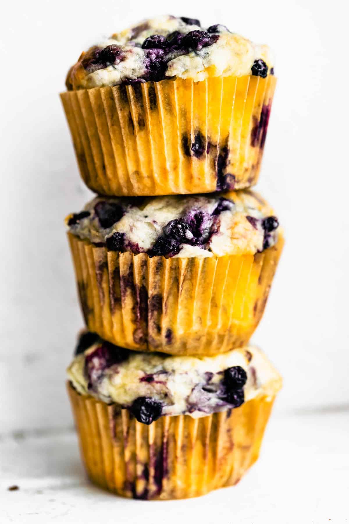 A stack of 3 gluten free blueberry muffins in muffin liners on top of each other.