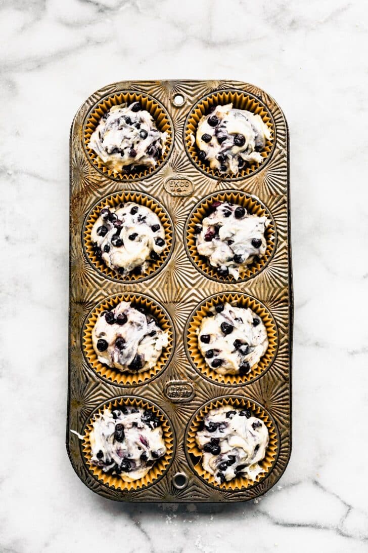 A muffin tin full of 8 unbaked gluten free blueberry muffins.