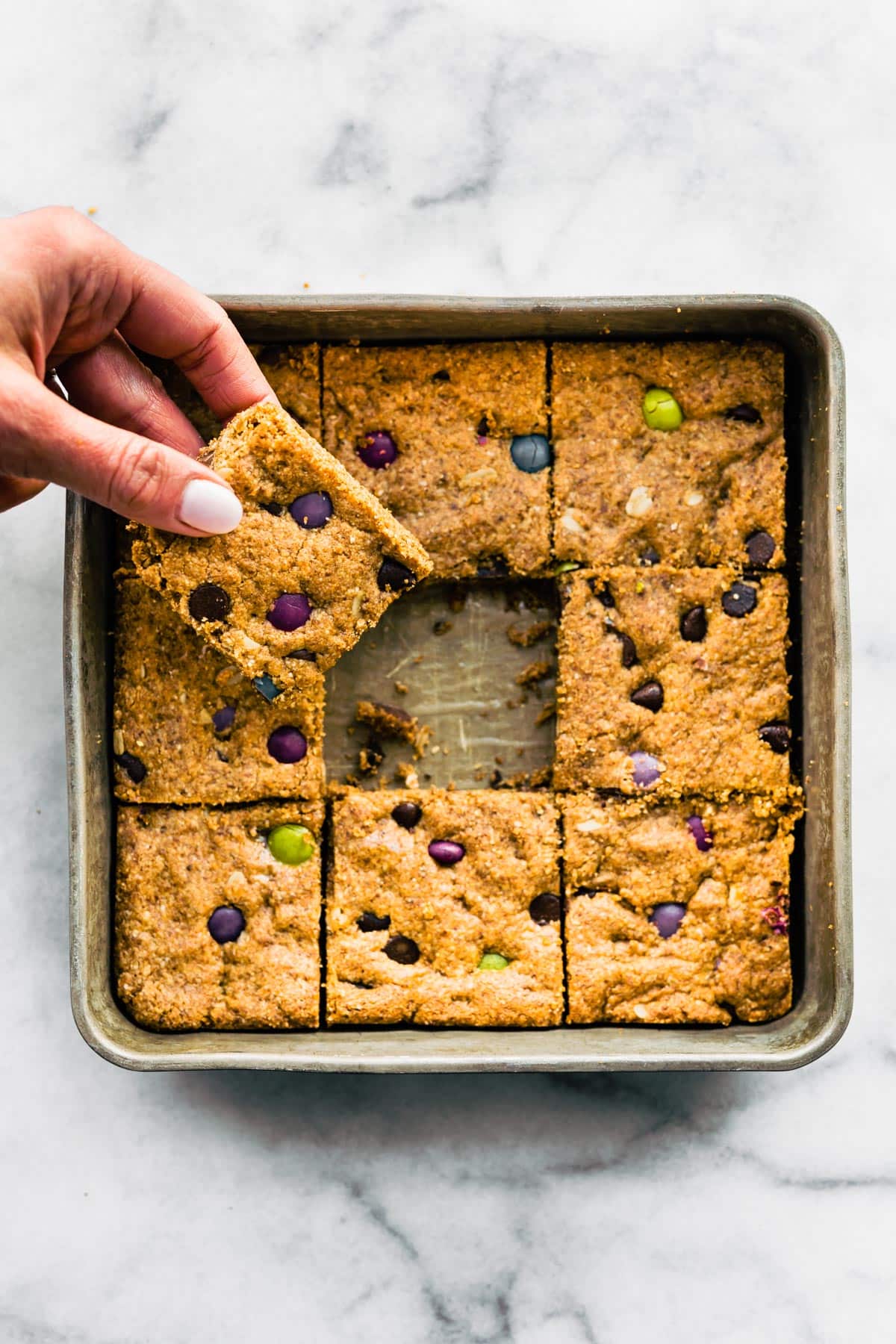 A hand grabbing a gluten free cookie bar from the middle of a pan of bars.