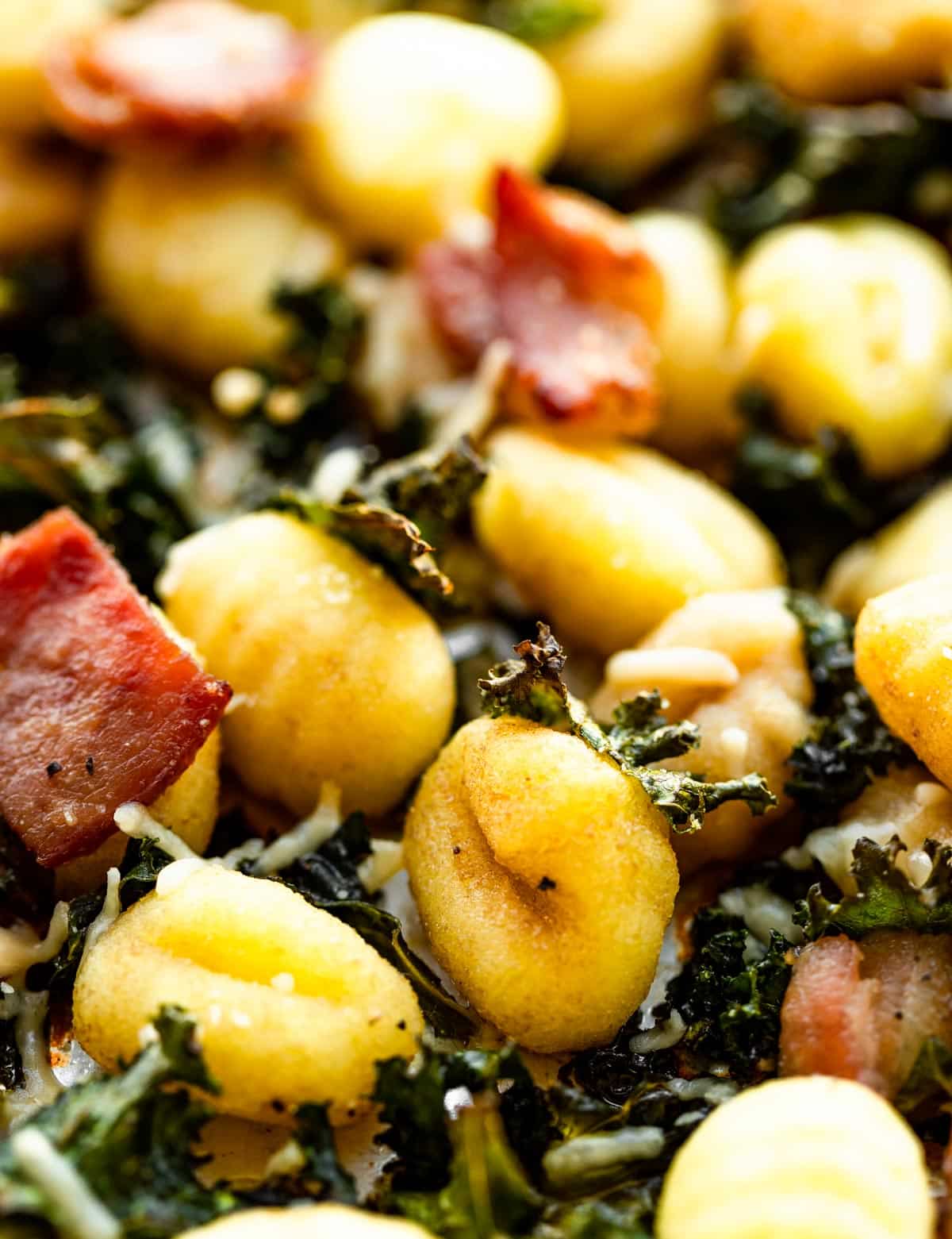 Close up image of sheet pan gluten-free baked gnocchi with kale, bacon, and Parmesan cheese.