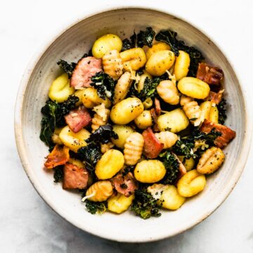 Overhead image of a bowl of sheet pan gluten-free baked gnocchi with kale, bacon, and Parmesan cheese.