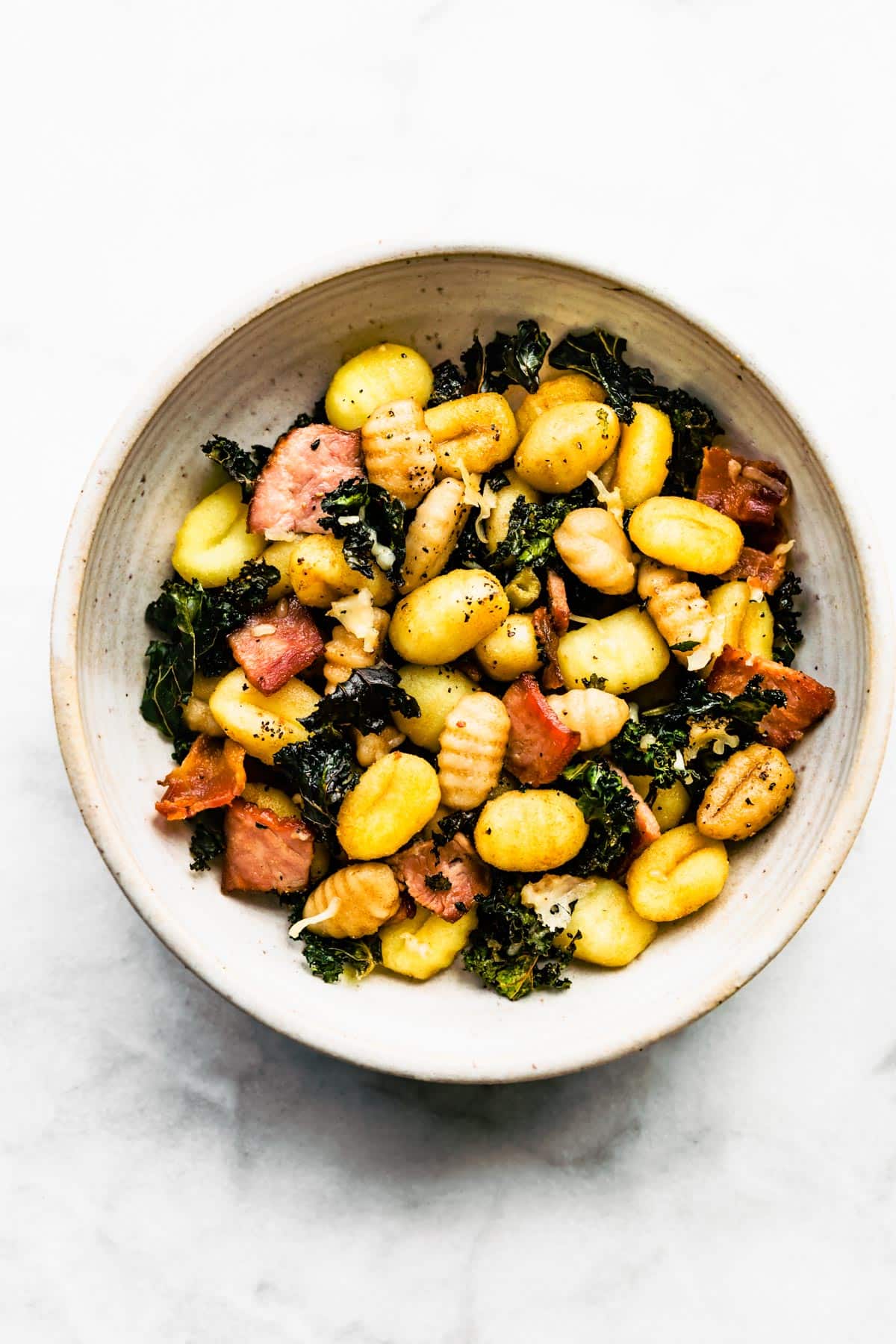 A bowl of gluten-free baked gnocchi with kale, bacon, and cheese.