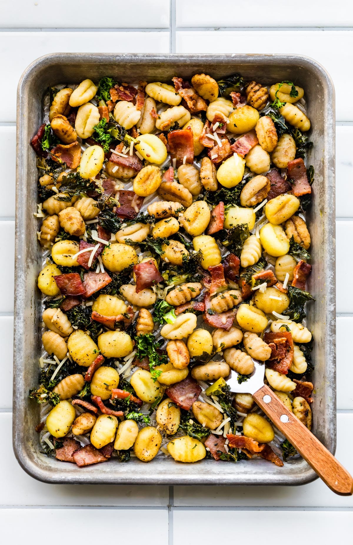 Gluten-Free Baked Gnocchi on a sheet pan with kale and bacon with a spatula sticking out. 