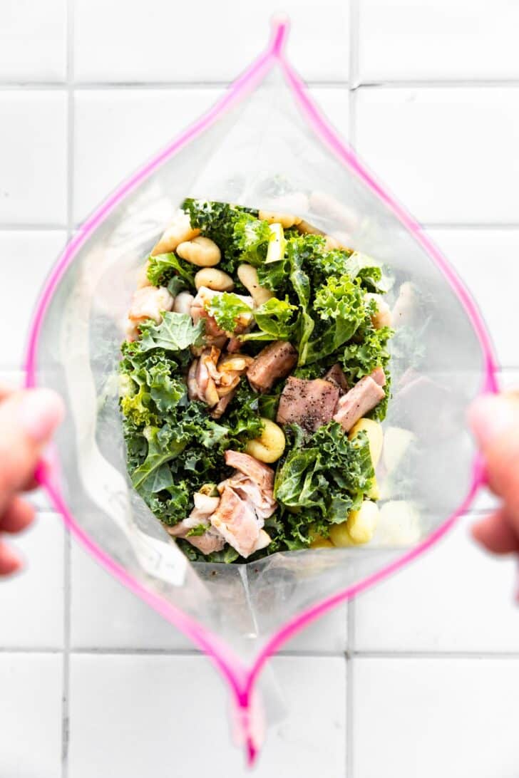 Overhead image of two hands holding a Ziploc bag with gluten-free gnocchi, bacon, and kale.