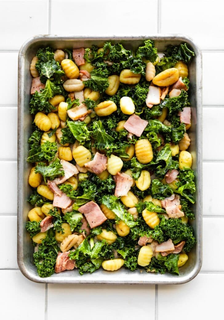 A sheet pan with uncooked gluten-free gnocchi, bacon, and kale.