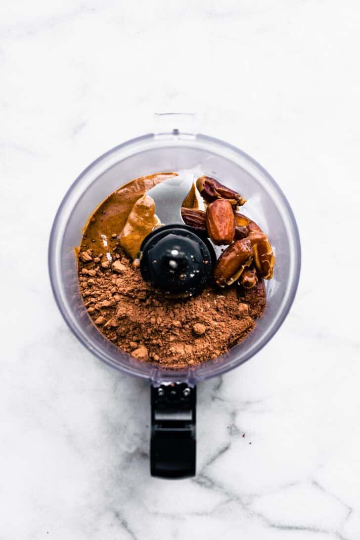 Overhead image of a food processor with dates sunflower seed butter, and cocoa powder.