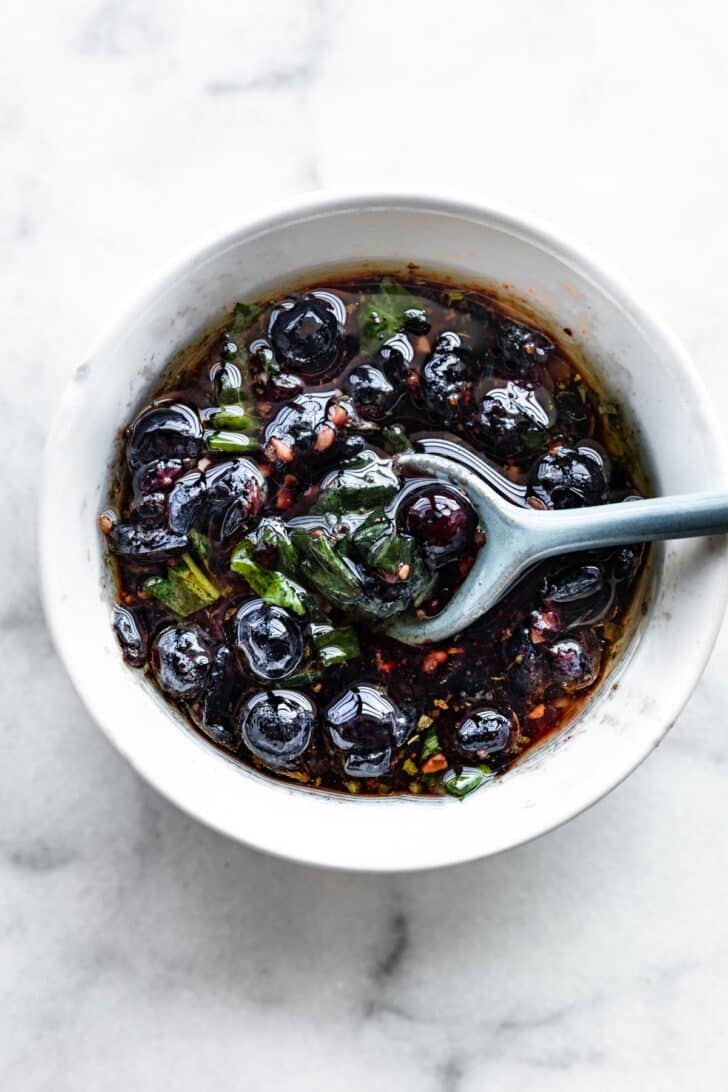 Overhead image of a bowl of an olive oil blueberry topping for salmon with a spoon dipping in.