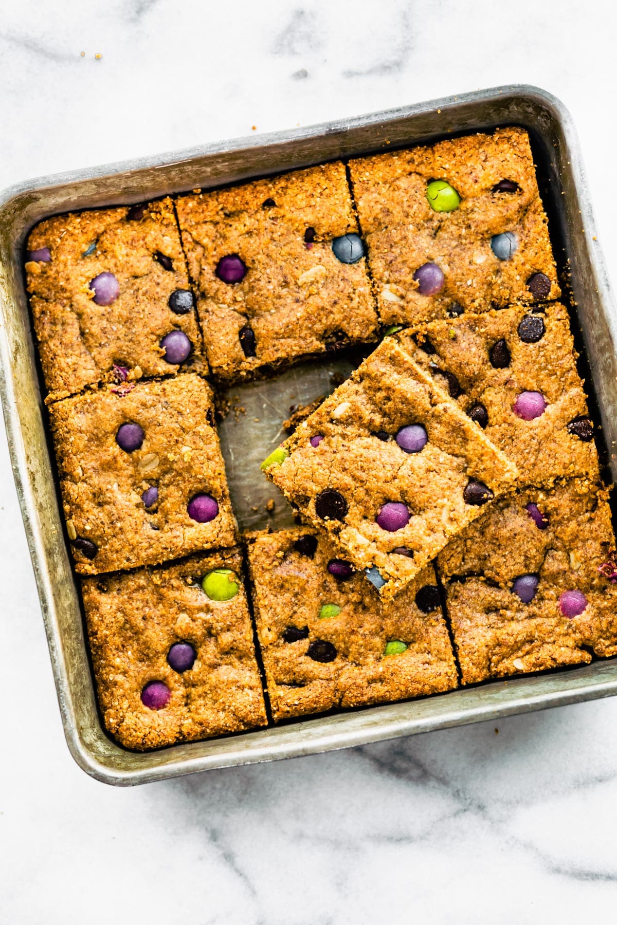 Overhead image of a pan of gluten free monster cookie bars with one removed and placed on top.