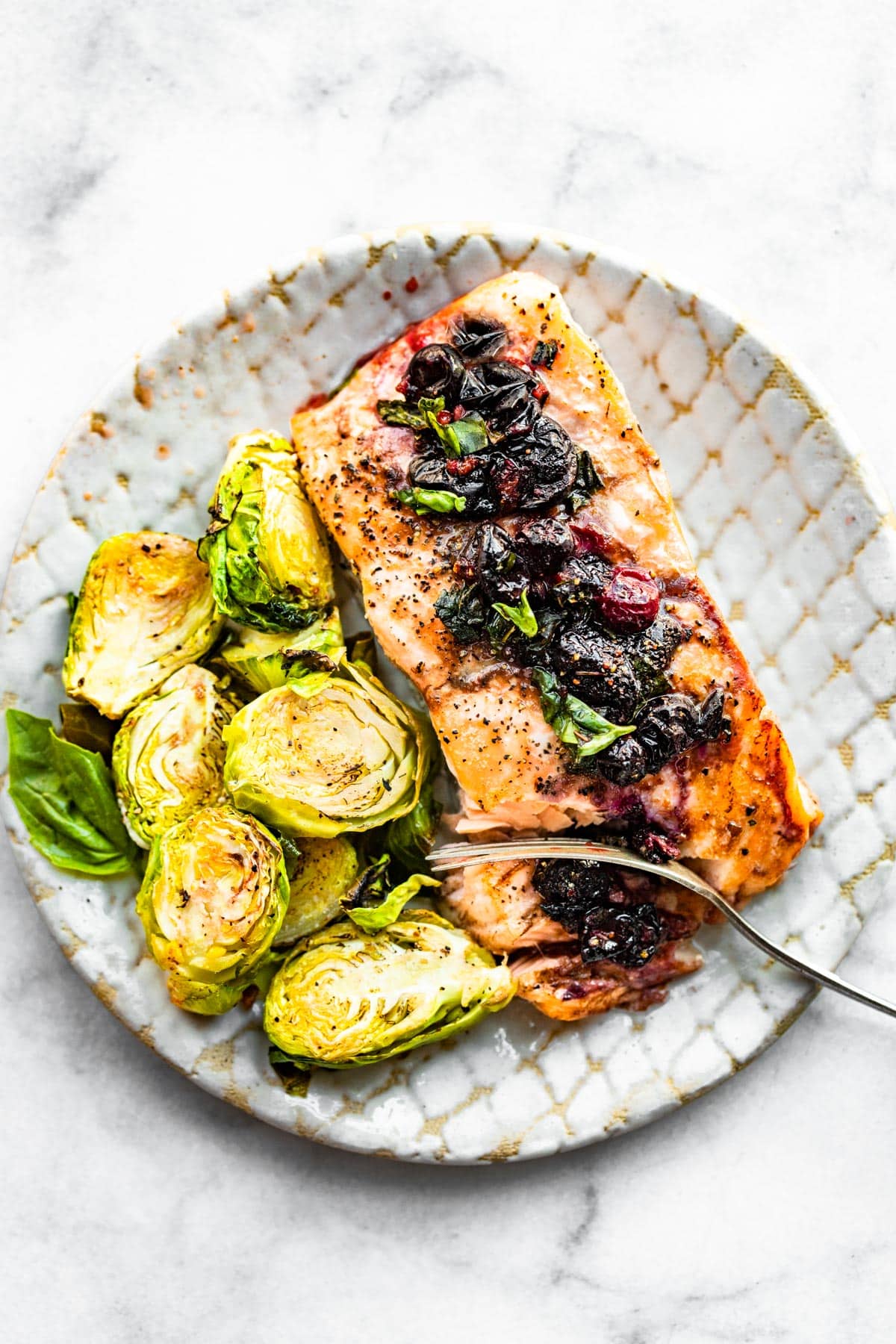 A plate with blueberry salmon and Brussels sprouts with a fork cutting a bite.