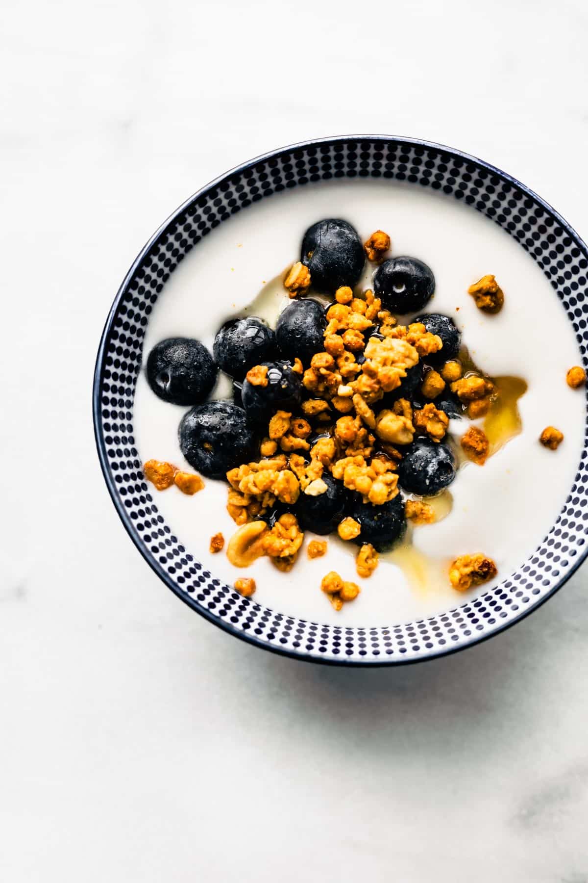 Overhead image of a bowl of coconut yogurt topped with blueberries, granola, and maple syrup.