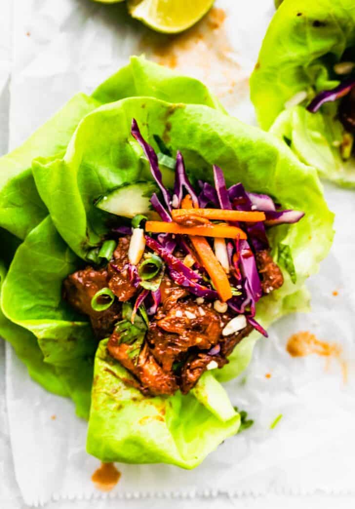 Overhead image of a BBQ Asian pork lettuce wrap topped with cabbage, carrots, and scallions.