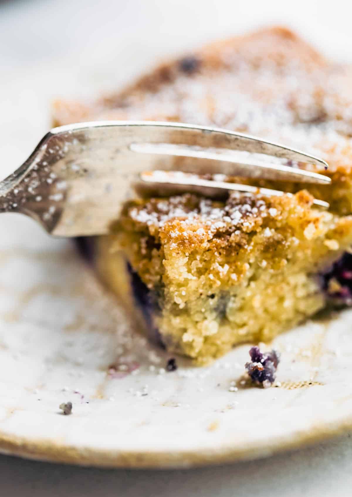 square pieces blueberry buckle coffee cake on white plate with fork in it.