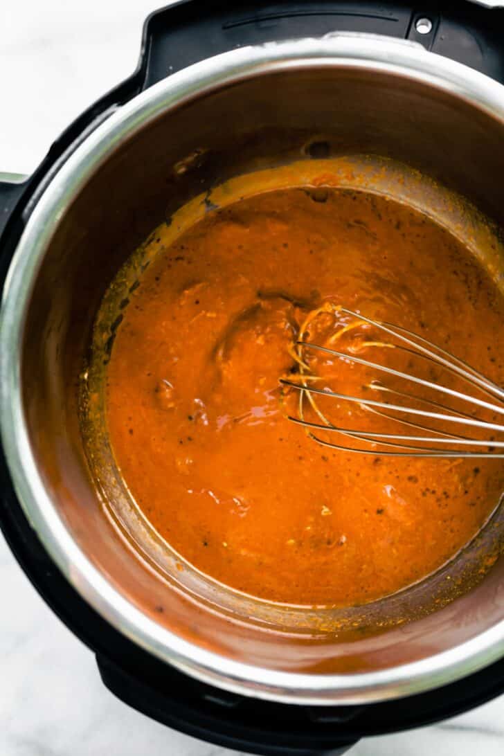 A whisk stirring ingredients in an Instant Pot to make sticky sweet Asian BBQ sauce.