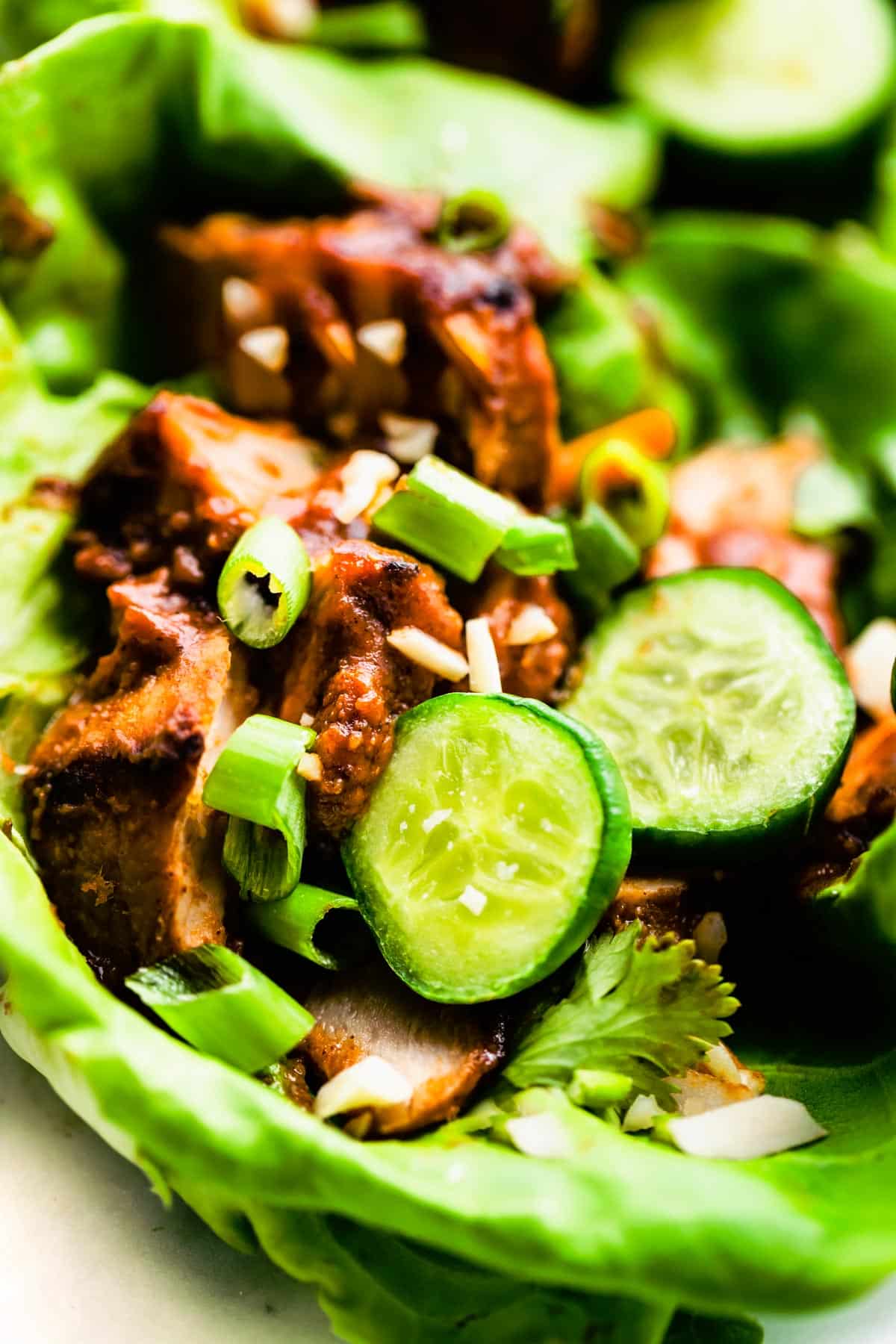 Close up image of BBQ pork in a lettuce wrap topped with scallions and cucumbers.