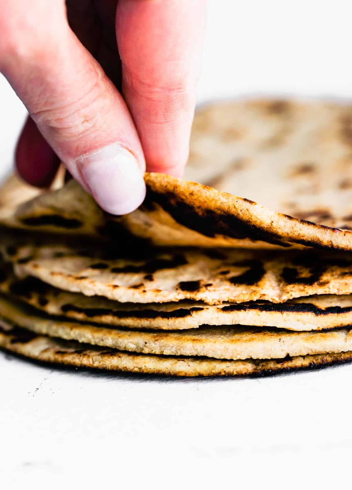 A hand grabbing an almond flour tortilla from a stack of tortillas.