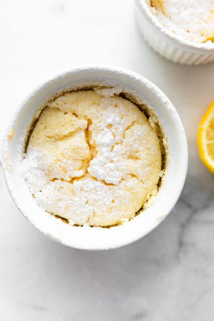 A gluten free lemon pudding cake in a ramekin topped with powdered sugar.