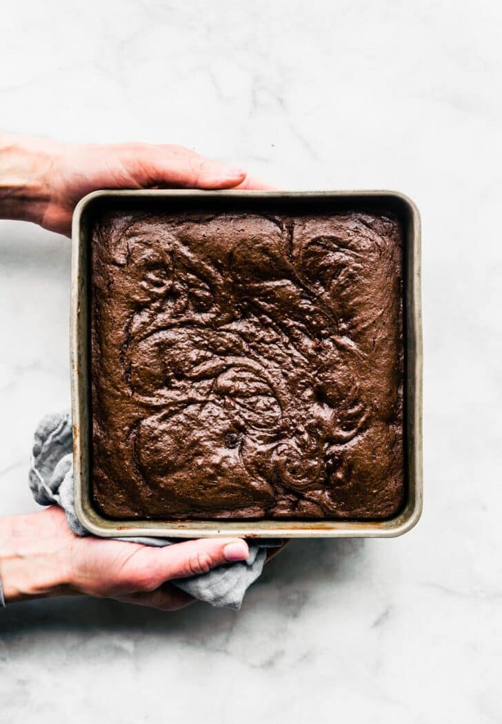 Two hands holding a square baking dish full of gluten free brownies.
