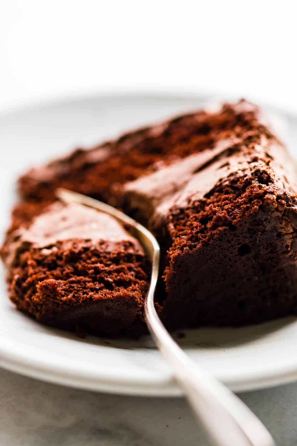 Close up image of a fork breaking into a slice of layered gluten free chocolate cake on a plate.