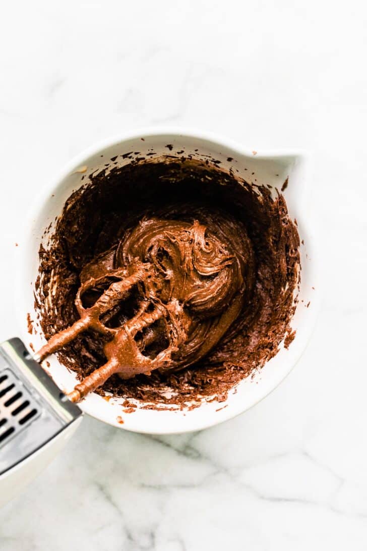 A hand mixer in a bowl with gluten free chocolate cake batter.