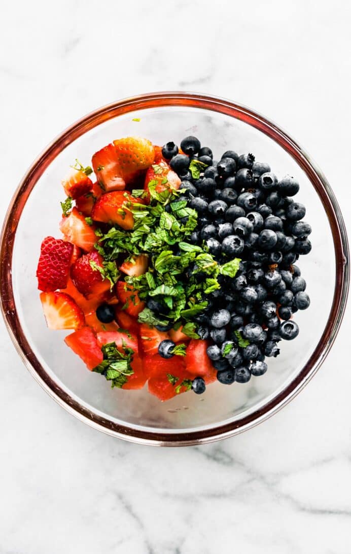 A large glass bowl with blueberries, strawberries, watermelon, and fresh mint.