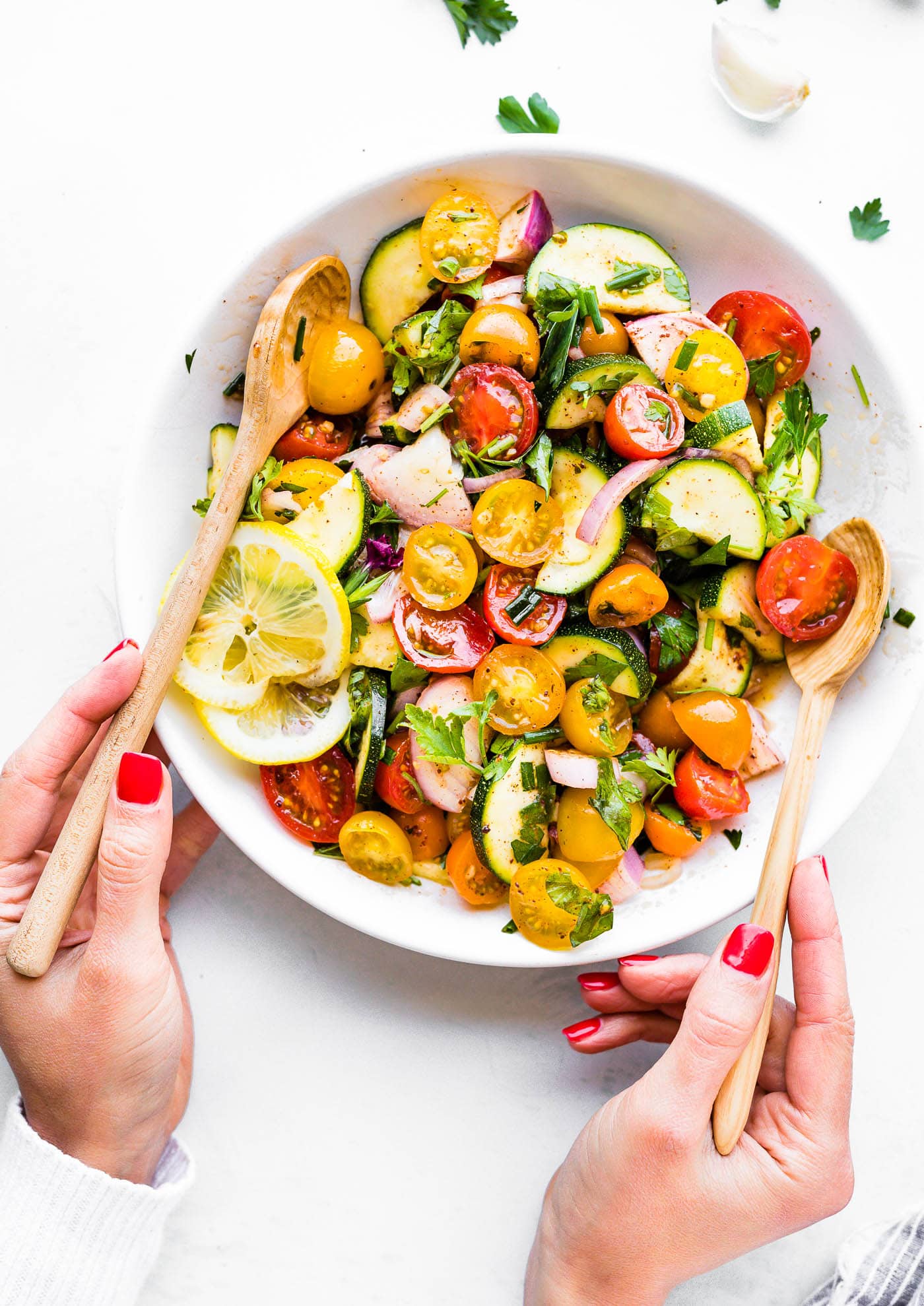 Two hands tossing a three herb tomato zucchini salad.