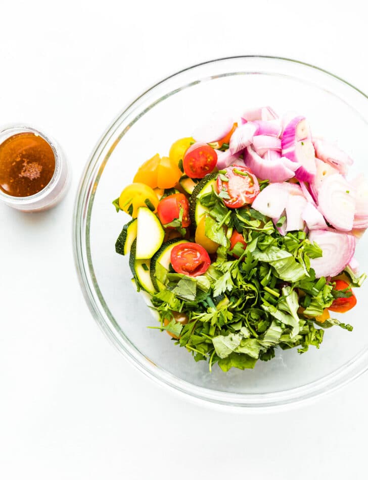 A bowl of three herb tomato zucchini salad and a jar of dressing on the side.