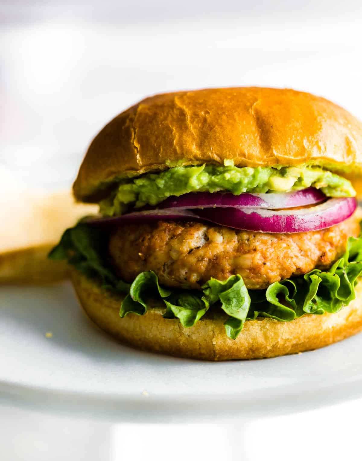 A grilled ground chicken burger with lettuce, red onion, and guacamole.