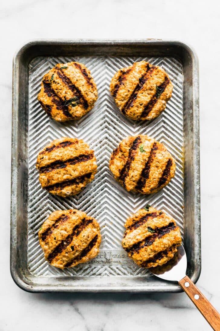 Six grilled ground chicken burgers on a baking sheet.