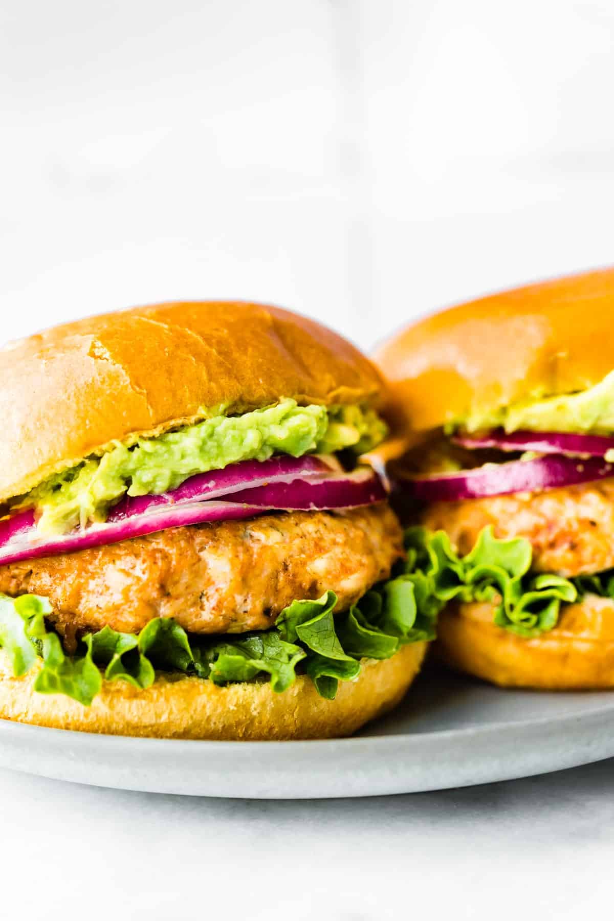 Two ground chicken burgers on buns with lettuce and red onion.