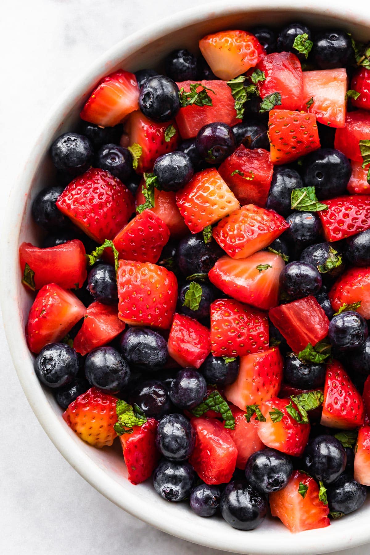 Close up image of a bowl of summer berry fruit salad with fresh herbs.