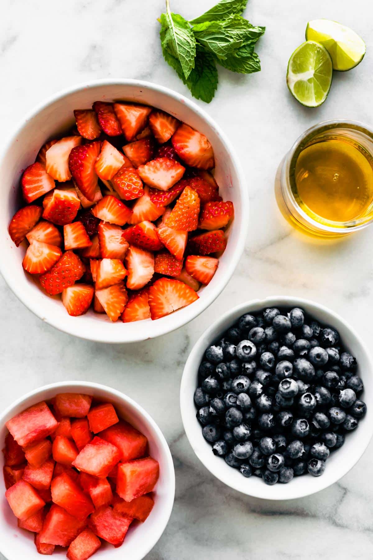 Ingredients to make a fresh summer berry salad including fruit, honey, limes, and herbs.