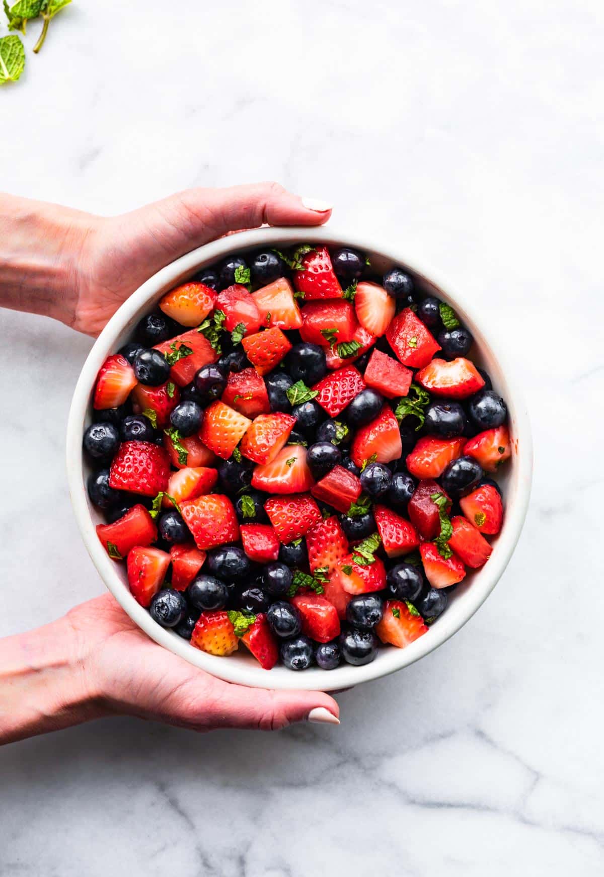 Two hands holding a bowl of summer berry fruit salad.