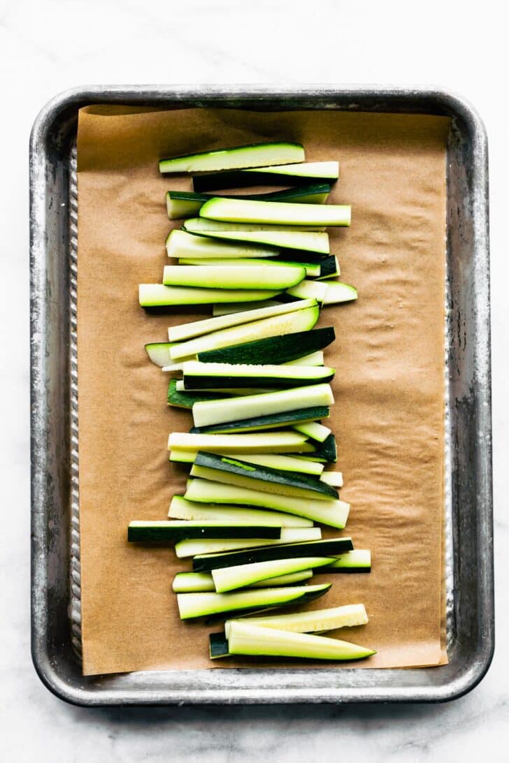 Raw zucchini sticks on a baking sheet lined with parchment paper.