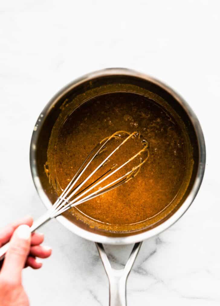 A honey and nut butter mixture in a metal sauce pan being whisked.