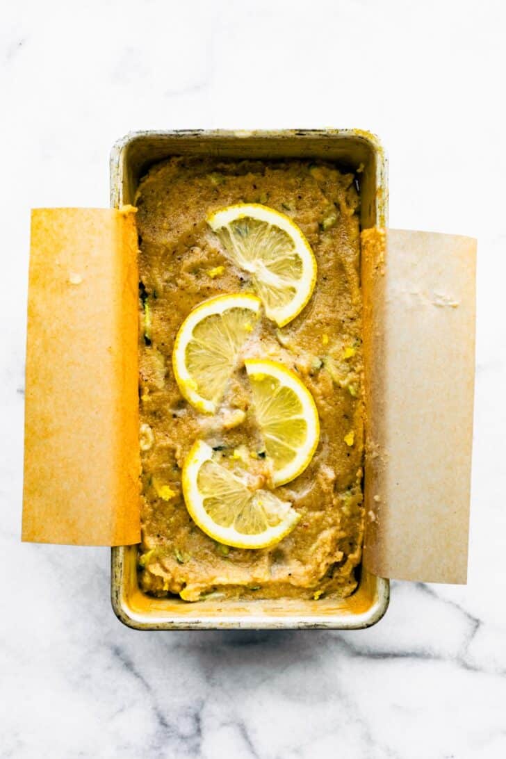 An unbaked loaf of lemon zucchini bread topped with lemon slices in a loaf pan.