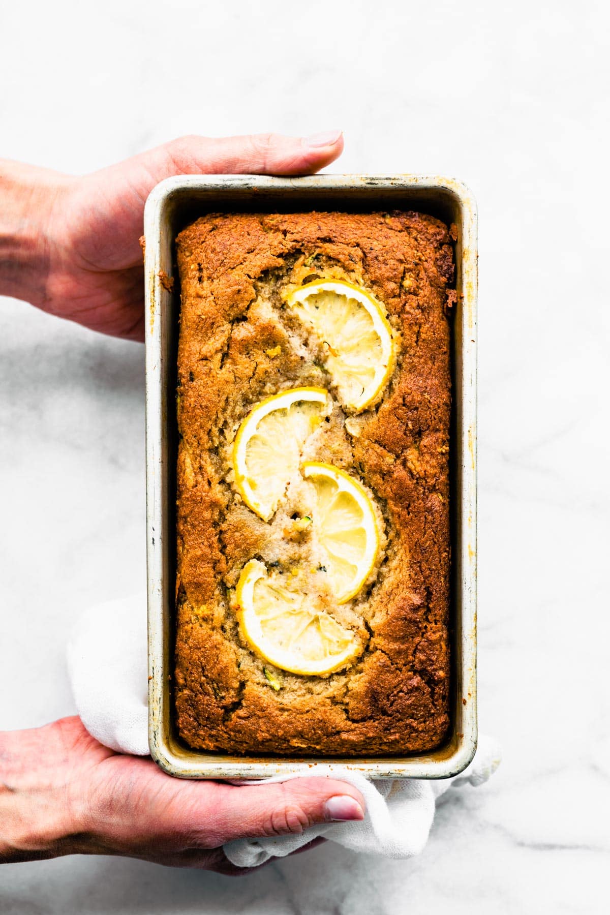 Two hands holding a baked loaf of lemon zucchini bread.