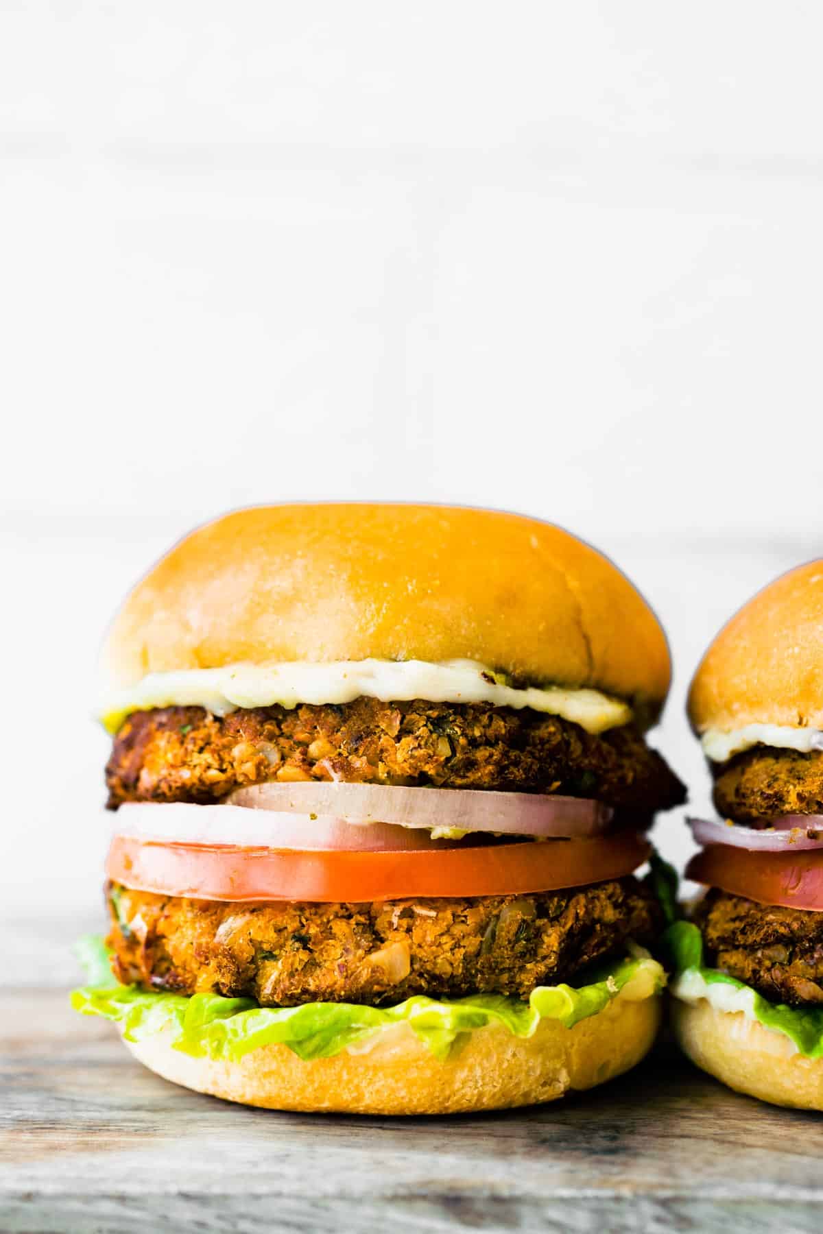 Two dairy free chickpea burgers on gluten free buns with red onion and tomato.