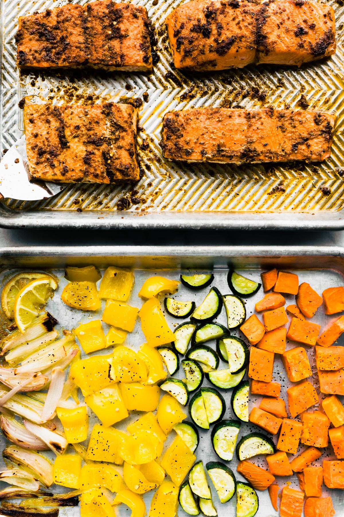 Two baking sheets, one with baked jerk salmon and one with roasted veggies.