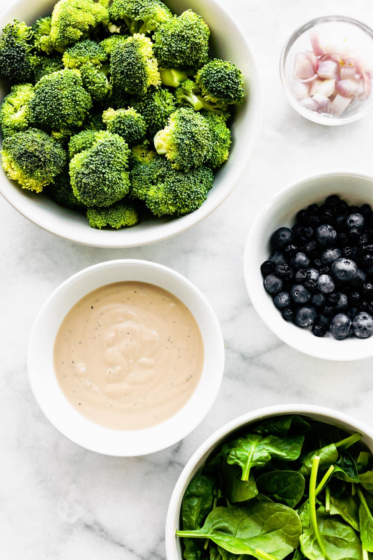 Fresh broccoli, blueberries and a creamy yogurt sauce in bowls on a marble countertop.