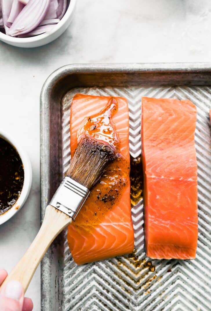 Brushing jerk marinade on salmon filets on a metal sheet pan.