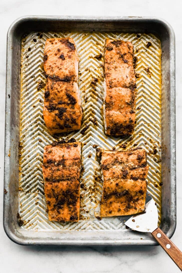A baking sheet with four pieces of baked salmon slathered in jerk marinade.