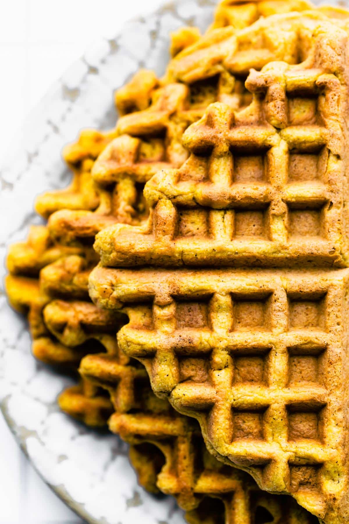Up close overhead photo of a stack of peanut butter waffles on a white plate.