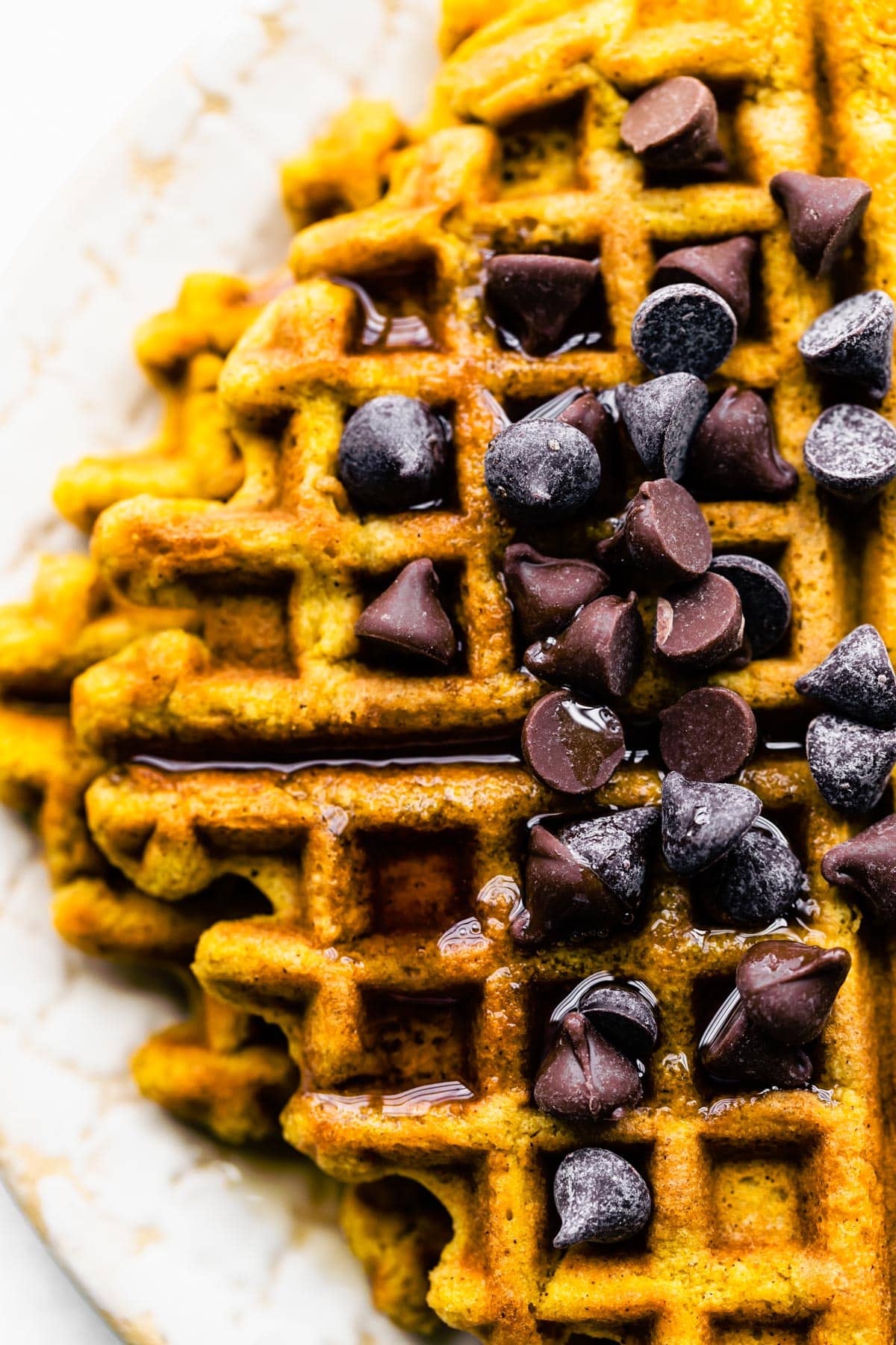 Overhead photo of flourless peanut butter waffles topped with chocolate chips and maple syrup.