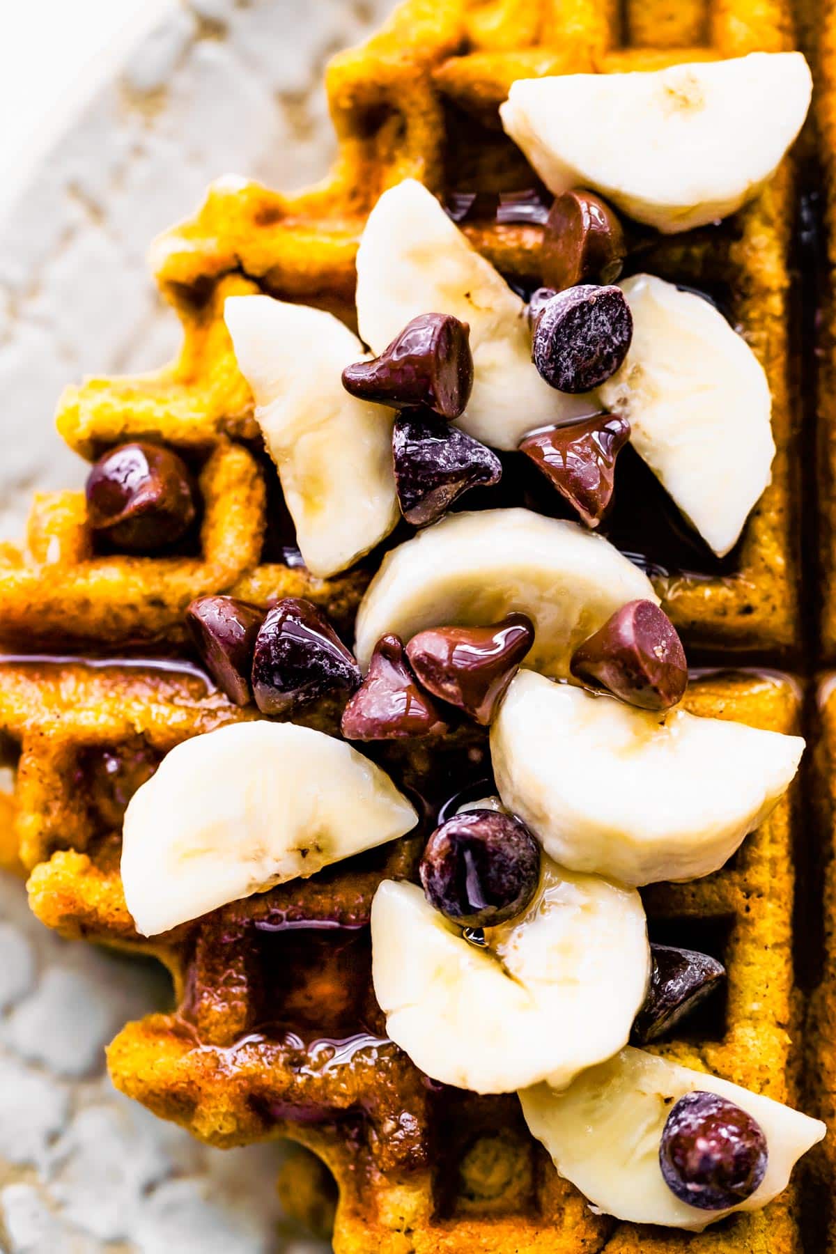 Overhead photo of flourless peanut butter waffles topped with banana slices and chocolate chips.