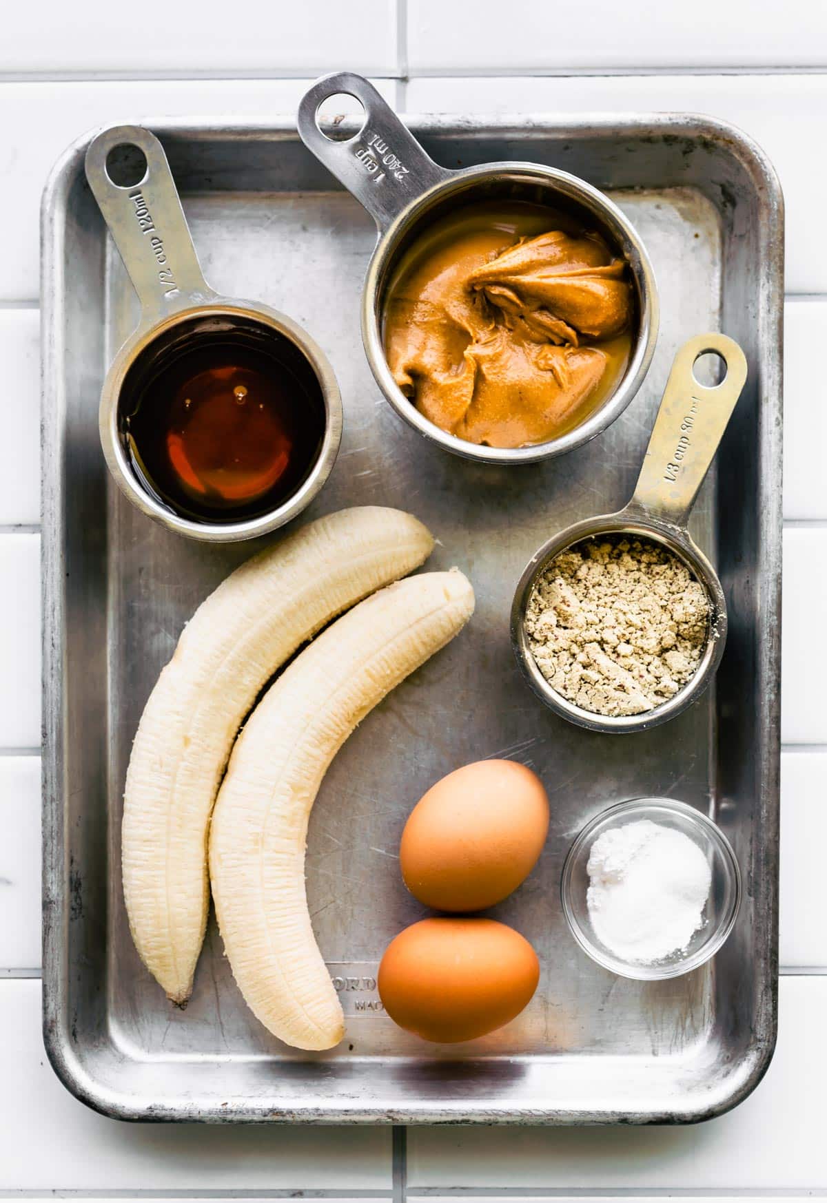 Peanut butter, bananas, maple syrup and eggs on a metal sheet pan.