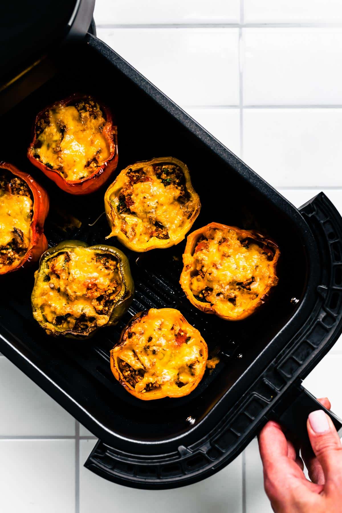 Six vegetarian stuffed bell peppers topped with melted cheese in an air fryer basket.