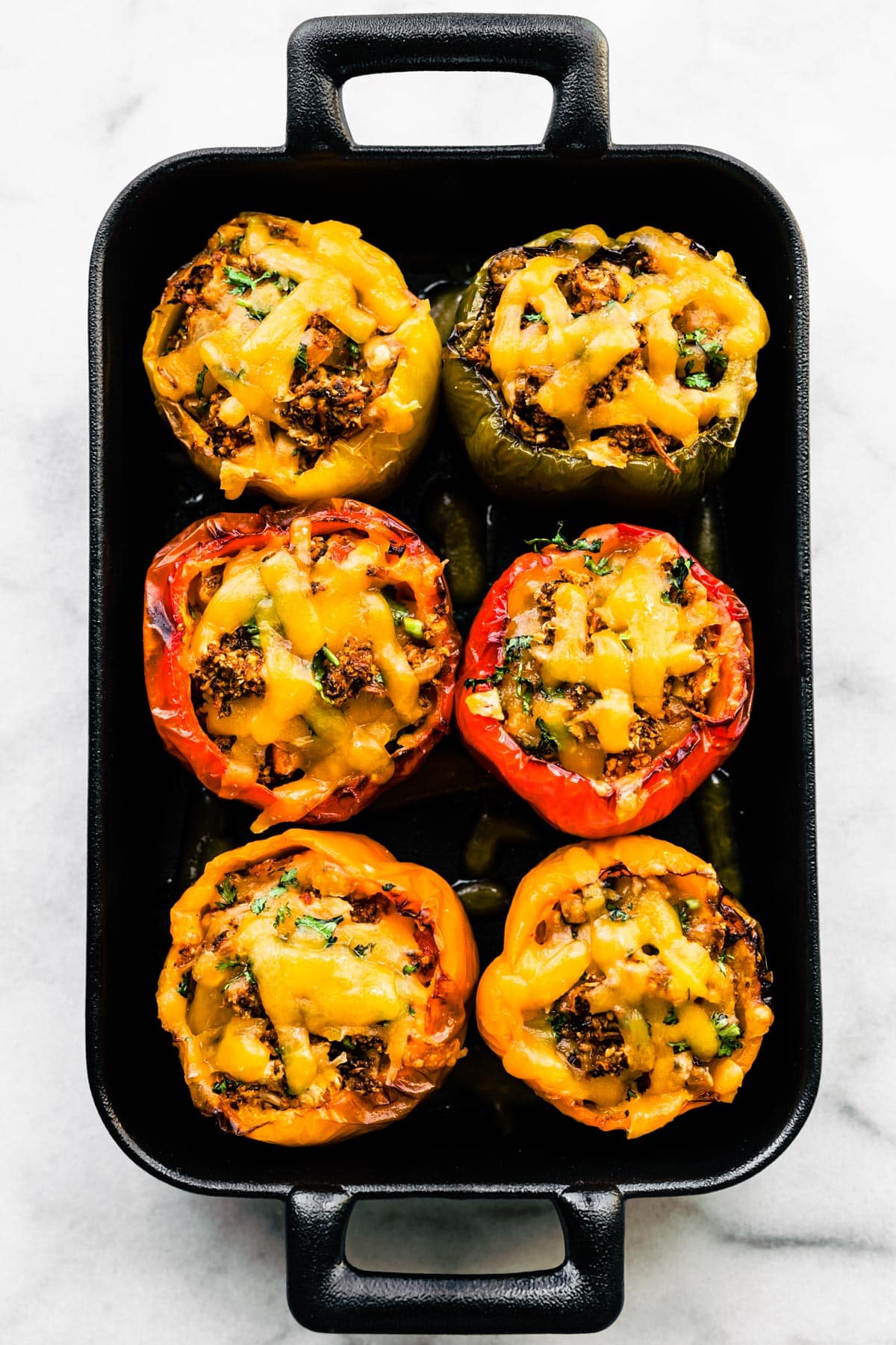 Overhead photo of six vegetarian stuffed bell peppers topped in a black casserole dish.