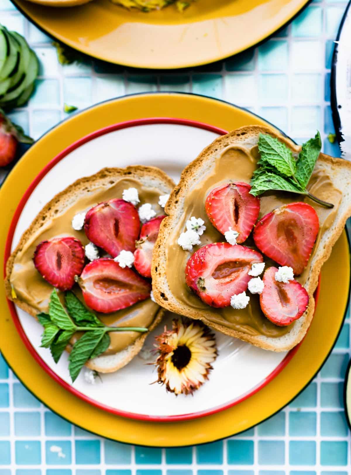 Two pieces of toast topped with homemade cashew butter. fresh strawberries and fresh mint.