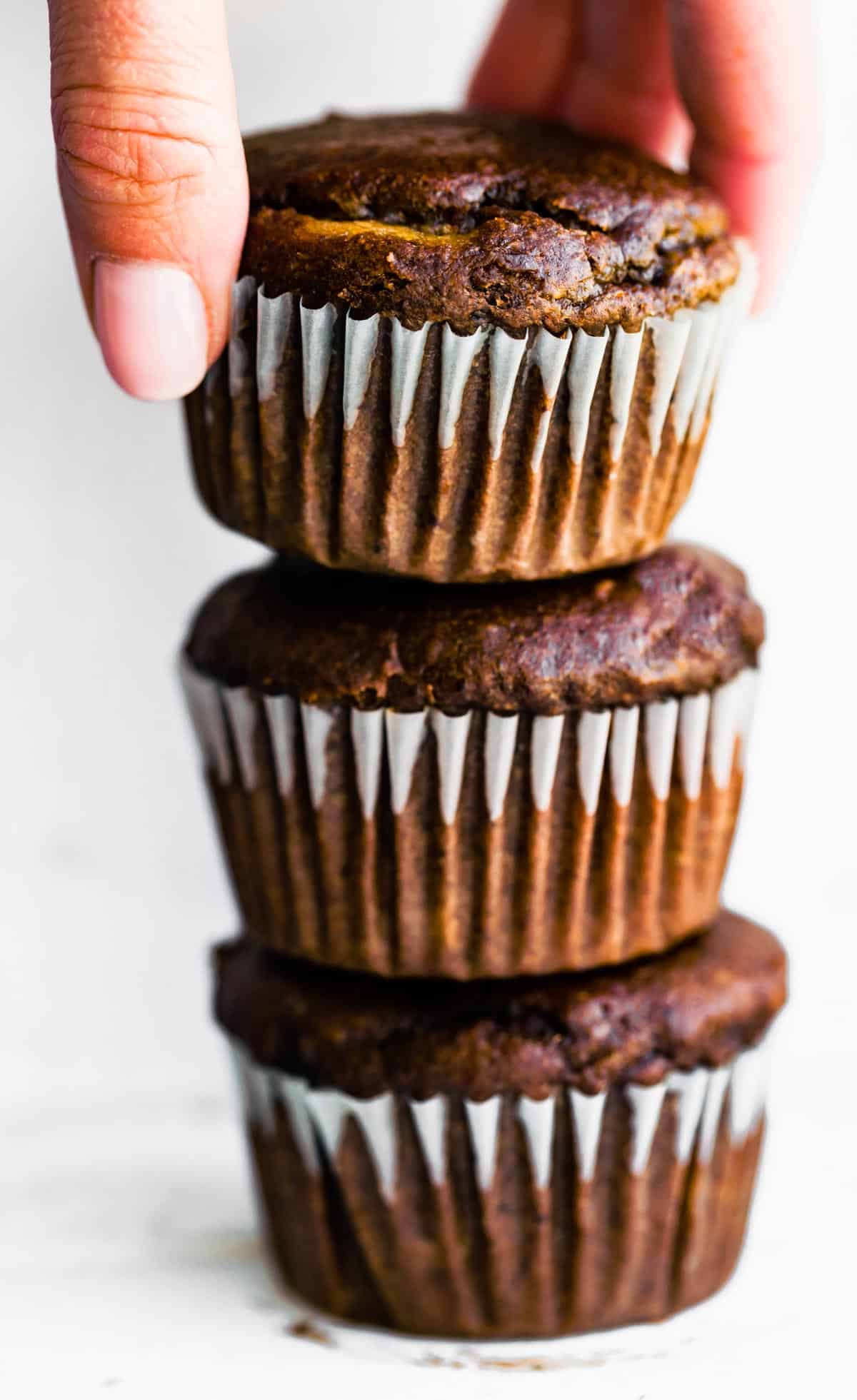 A woman's hand reaching for the top muffin stacked on two other healthy banana muffins.